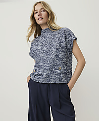 A woman in a textured blue top and dark pants stands against a plain, light gray background. carousel Product Image 1