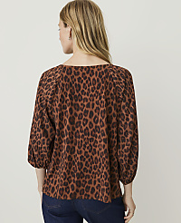 A woman in a brown leopard-print top and dark jeans stands against a plain white background. carousel Product Image 2