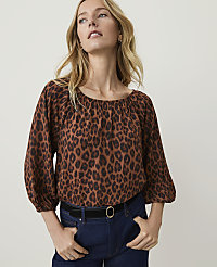 A woman in a leopard print blouse and dark jeans stands against a plain, light background. carousel Product Image 1