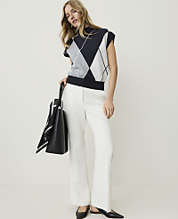 A woman in a sleeveless argyle sweater and white pants stands with a black tote bag against a plain white background. carousel Product Image 4