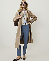 A woman in a floral top, blue trousers, and a trench coat stands against a plain white background. carousel Product Image 4
