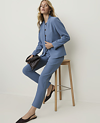 A woman in a blue suit sits on a stool, holding a woven bag, against a plain white background. carousel Product Image 3