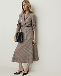 A woman in a patterned suit and heels stands holding a black handbag against a plain, light-colored wall. carousel Product Image 1