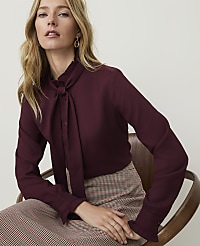 A woman in a burgundy pussy-bow blouse and plaid skirt sits against a plain, light background. carousel Product Image 1