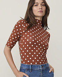 A woman in a brown polka dot turtleneck and blue jeans stands against a plain, light-colored background. carousel Product Image 1