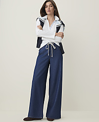 A woman in a white polo shirt and wide-leg jeans stands with her arms crossed against a plain, light-colored background. carousel Product Image 1