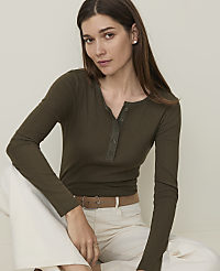 A woman in a green henley shirt and white pants sits against a plain, light background. carousel Product Image 1