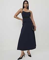 A woman in a navy blue dress and black heels stands against a plain white background, holding a black clutch. carousel Product Image 1