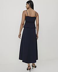 A woman in a navy blue dress with spaghetti straps and a black waistband stands against a plain white background. carousel Product Image 2