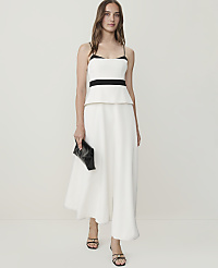 A woman in a white peplum top and wide-leg pants holds a black clutch against a plain white background. carousel Product Image 1
