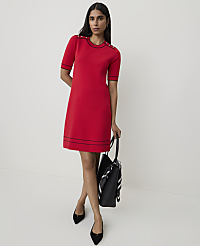 A woman in a red dress stands against a plain white background, holding a black tote bag. carousel Product Image 2