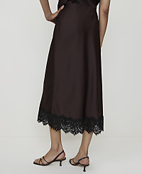 A person stands in front of a plain white background, wearing a brown satin skirt with a black lace hem and strappy sandals. carousel Product Image 3