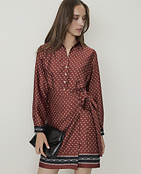A woman in a patterned rust-colored dress with a black clutch stands against a plain white background. carousel Product Image 3