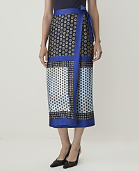 A woman models a patterned wrap skirt with a blue border, standing against a plain, light-colored background. carousel Product Image 2
