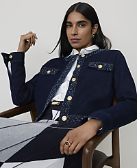 A woman in a denim jacket and patterned skirt sits in a chair against a plain background. carousel Product Image 1