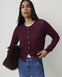 A woman in a burgundy cardigan and jeans stands against a plain background, holding a dark brown bag. carousel Product Image 1