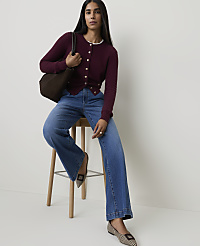 A woman in a burgundy cardigan and wide-leg jeans sits on a stool with a brown tote bag, against a plain white background. carousel Product Image 3