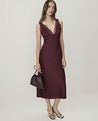 A woman in a burgundy slip dress with lace trim and a woven handbag stands against a plain white background. carousel Product Image 1