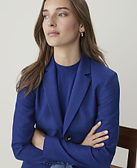 A woman in a blue blazer with her arms crossed is looking away from the camera against a plain, light-colored background. carousel Product Image 4