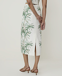 A person stands in the foreground wearing a white skirt with a green tropical leaf pattern, while the background is a plain, light-colored wall. carousel Product Image 3