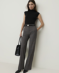 A woman in a black turtleneck and plaid pants stands against a plain white wall, holding a black tote bag. carousel Product Image 4