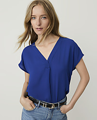 A woman in a blue v-neck top and jeans stands against a plain white background. carousel Product Image 1