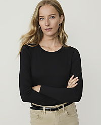 A woman with blonde hair and hoop earrings, wearing a black long-sleeved shirt and tan pants, stands with her arms crossed against a plain white background. carousel Product Image 1