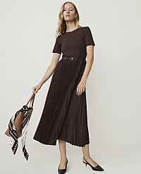 A woman in a brown pleated dress and matching top stands against a plain white background, holding a brown tote bag with a patterned scarf. carousel Product Image 1