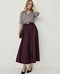 A woman in a striped shirt and burgundy skirt stands against a plain white background, holding a brown clutch. carousel Product Image 3