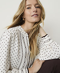 A blonde woman in a patterned blouse and brown pants poses against a plain background. carousel Product Image 1