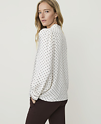 A woman in a white polka-dot blouse and brown pants stands against a plain, light background. carousel Product Image 3