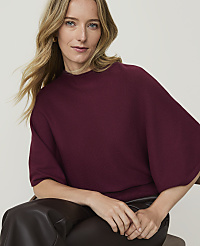 A woman with blonde hair wearing a maroon sweater and dark pants sits in front of a blurred background. carousel Product Image 3