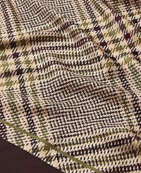 A close-up of a wrinkled fabric with a brown, green, and beige plaid pattern fills the foreground, while a dark brown border is visible at the bottom left. carousel Product Image 2