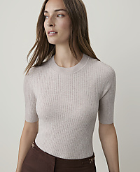A woman in a beige ribbed sweater and brown skirt stands against a plain, light gray background. carousel Product Image 1