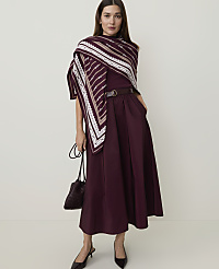 A woman in a burgundy dress and patterned scarf stands against a plain, light background, holding a dark handbag. carousel Product Image 1