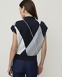 A woman in a navy, white, and gray argyle sweater vest and dark jeans stands against a plain, light gray background. carousel Product Image 2