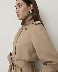 A woman in a tan trench coat with a tie at the waist is shown in profile against a plain white background. carousel Product Image 1