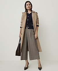 A woman in a trench coat and plaid culottes stands against a plain, light-colored background, holding a dark tote bag. carousel Product Image 4