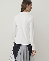 A woman in a white collared shirt and a pleated skirt stands against a plain white background. carousel Product Image 1
