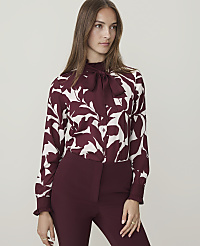A woman in a maroon and white floral blouse and maroon pants stands against a plain, light gray background. carousel Product Image 1