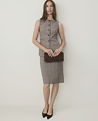 A woman in a plaid vest and skirt holds a brown clutch in front of a plain, light-colored wall. carousel Product Image 1
