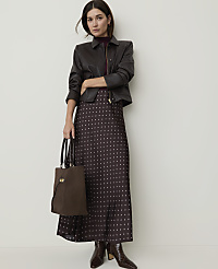 A woman in a patterned skirt and leather jacket stands with a handbag against a plain wall. carousel Product Image 1