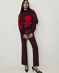 A woman in a burgundy sweater with a red floral print and matching pants holds a clutch in front of a plain white background. carousel Product Image 3