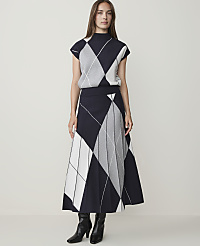 A woman in a navy, white, and gray argyle knit top and pleated skirt stands against a plain, light gray background. carousel Product Image 1