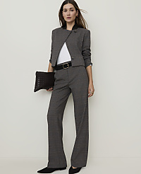 A woman in a grey plaid suit and black heels stands holding a dark woven clutch against a plain white background. carousel Product Image 1