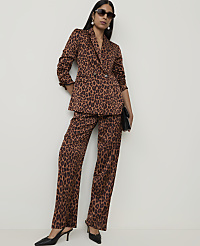 A woman in a leopard print suit stands against a plain white wall, holding a black clutch. carousel Product Image 1