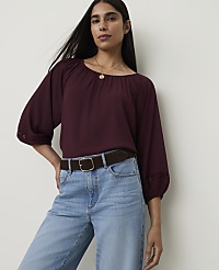 A woman in a burgundy blouse and light wash jeans stands against a plain white background. carousel Product Image 1
