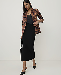 A woman in a leopard print blazer and black skirt stands against a plain, light background, holding a black tote bag. carousel Product Image 3