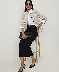 A woman in a tweed jacket and black skirt sits on a stool in front of a plain white background. carousel Product Image 3