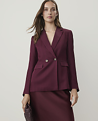 A woman in a burgundy blazer and skirt holds a textured clutch in front of a plain, light-colored background. carousel Product Image 1